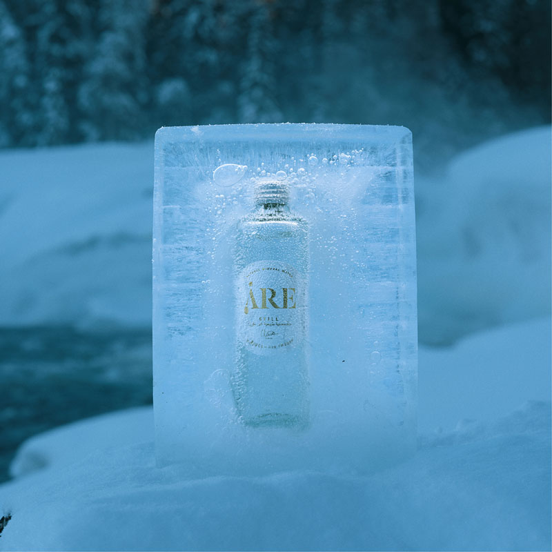 Åre water bottle frozen inside a transparent block of ice, resting on a snow-covered rock in a chilly Nordic winter landscape.